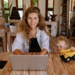 mãe empreendedora - mão trabalhando no notebook enqaunto filho pequeno brinca de carrinho