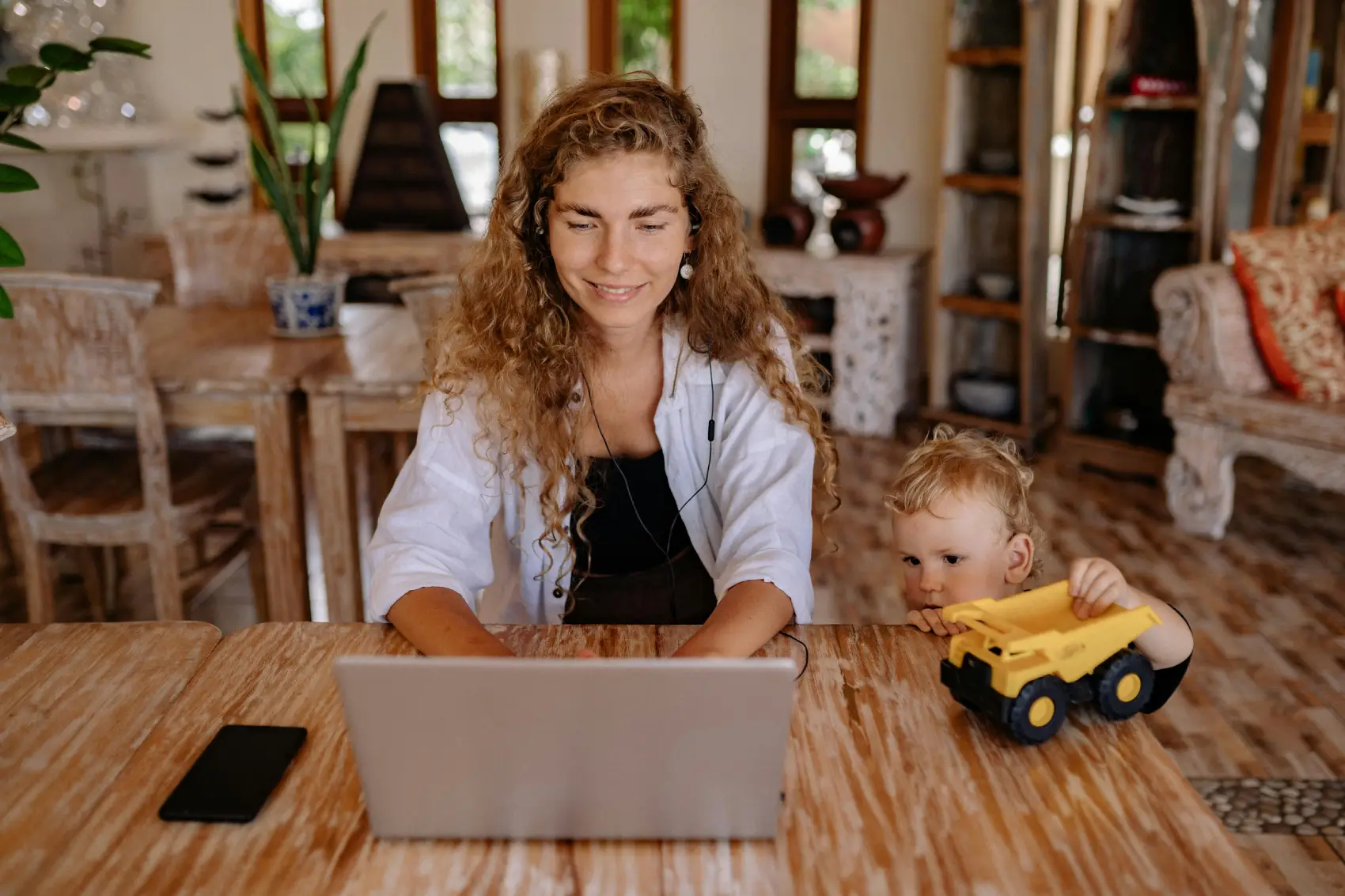 mãe empreendedora - mão trabalhando no notebook enqaunto filho pequeno brinca de carrinho
