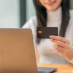 como vender parcelado - Um close-up de uma mulher de negócios segurando um cartão de crédito enquanto usa um laptop em um espaço de trabalho moderno