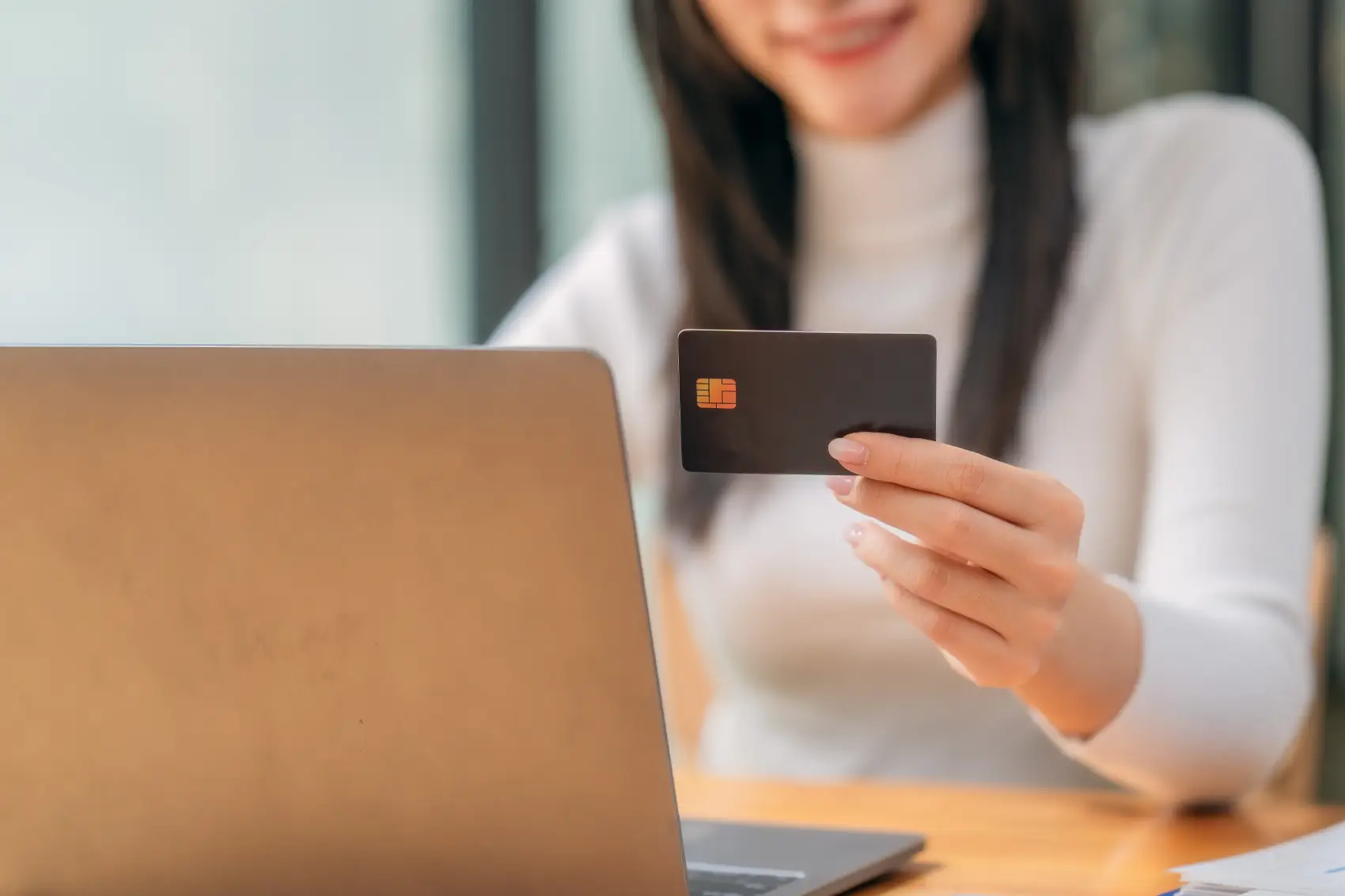 como vender parcelado - Um close-up de uma mulher de negócios segurando um cartão de crédito enquanto usa um laptop em um espaço de trabalho moderno