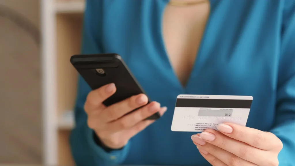 mão feminina segurando cartão e celular