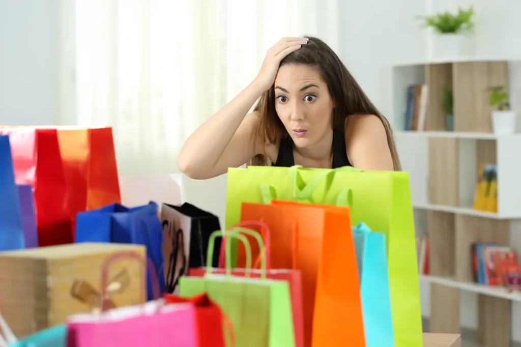 arrependimento de compra - mulher surpresa olhando para várias compras em sacolas coloridas em casa