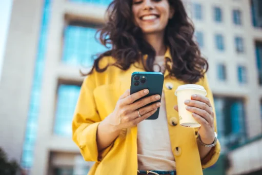 o que é conta digital - Jovem empresária de atitude positiva, com um copo de café para viagem na mão, usando o celular