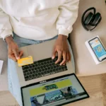 cupom-loja-online homem olhando cartão e com notebook no colo definindo sua compra online