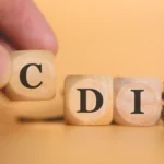 o que é cdi​ - Um homem formando a sigla CDI escrita em dados de madeira em uma foto de estúdio com moedas na composição
