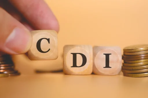 o que é cdi​ - Um homem formando a sigla CDI escrita em dados de madeira em uma foto de estúdio com moedas na composição