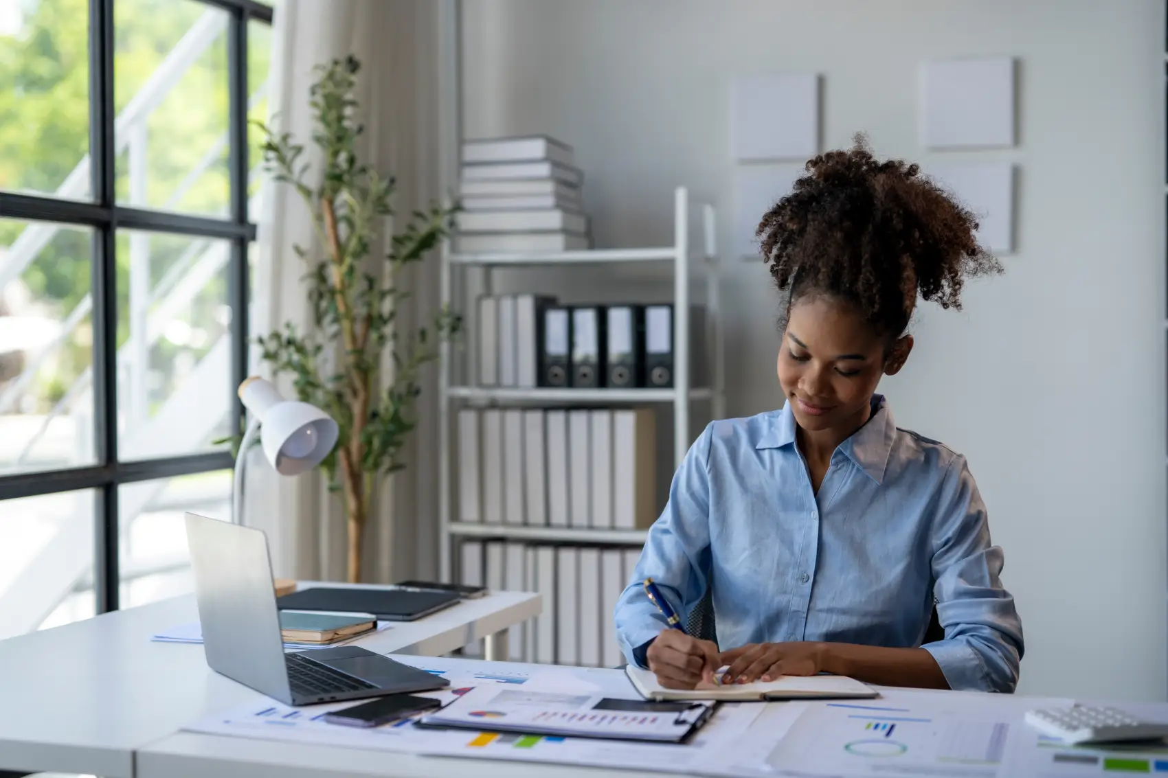 como regularizar o mei - mulher preta com coque sentada à mesa com um notebook e um caderno, sorrindo