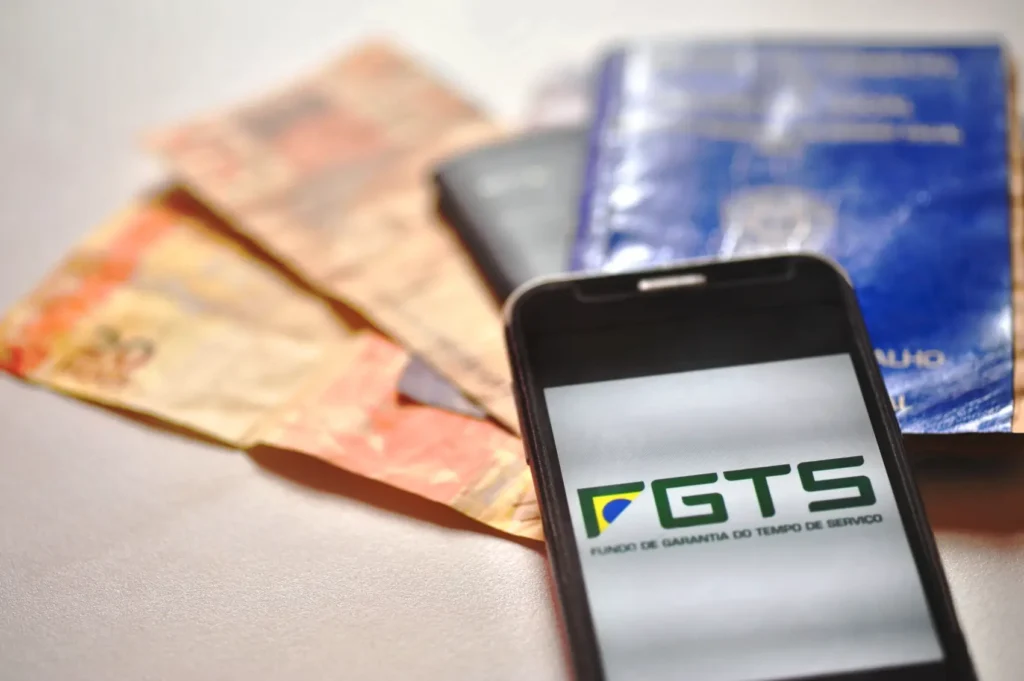 guia-do-fgts notas de dinheiro, cartão, carteira de trabalho e celular com aplicativo do FGTS