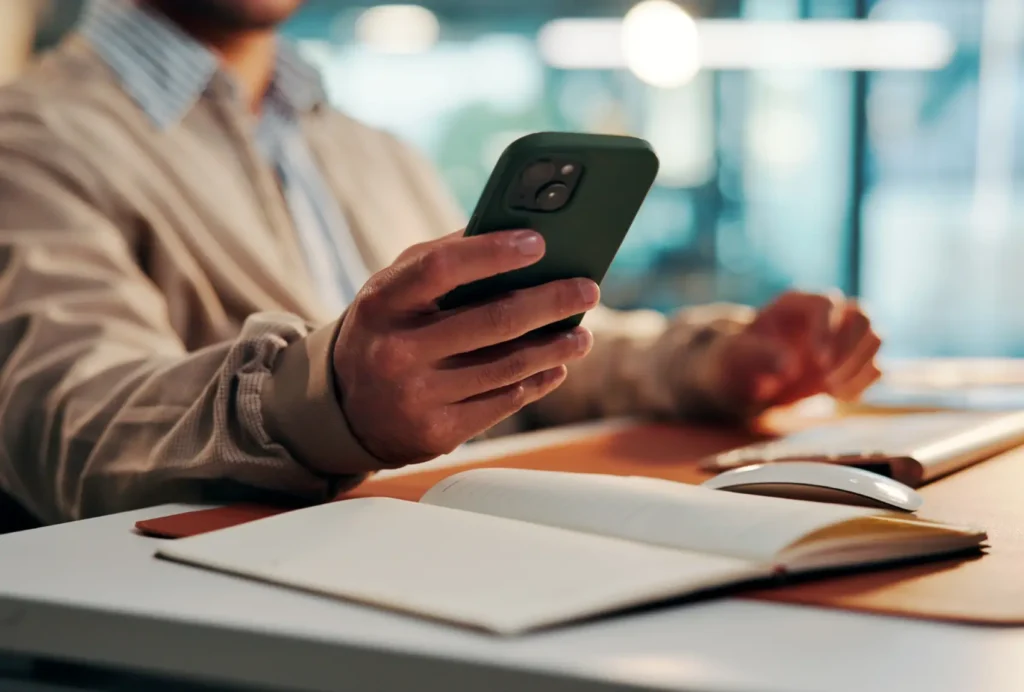 o que é ETF - mãos de homem de negócios olhando o celular com caderno aberto sobre a mesa