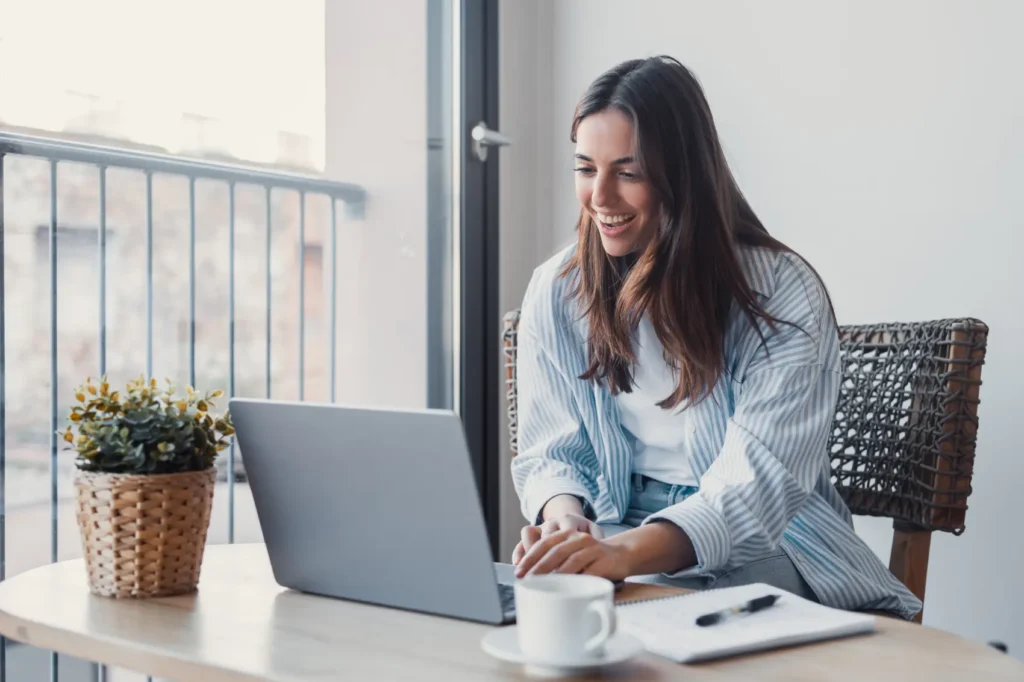 darf-e-imposto-de-renda Mulher positiva conversando com o cliente em uma chamada de vídeo no laptop, tomando notas, falando no computador, sentando na mesa de trabalho, usando dispositivos para comunicação de trabalho
