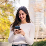 conta rendeira - Mulher caucasiana sorrindo feliz enquanto usa seu celular