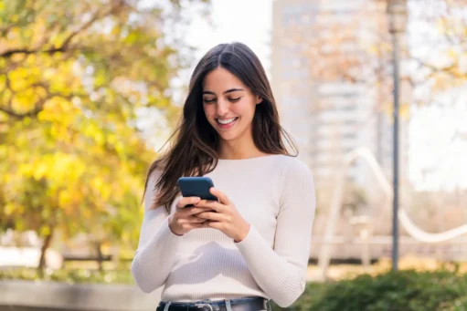 conta rendeira - Mulher caucasiana sorrindo feliz enquanto usa seu celular