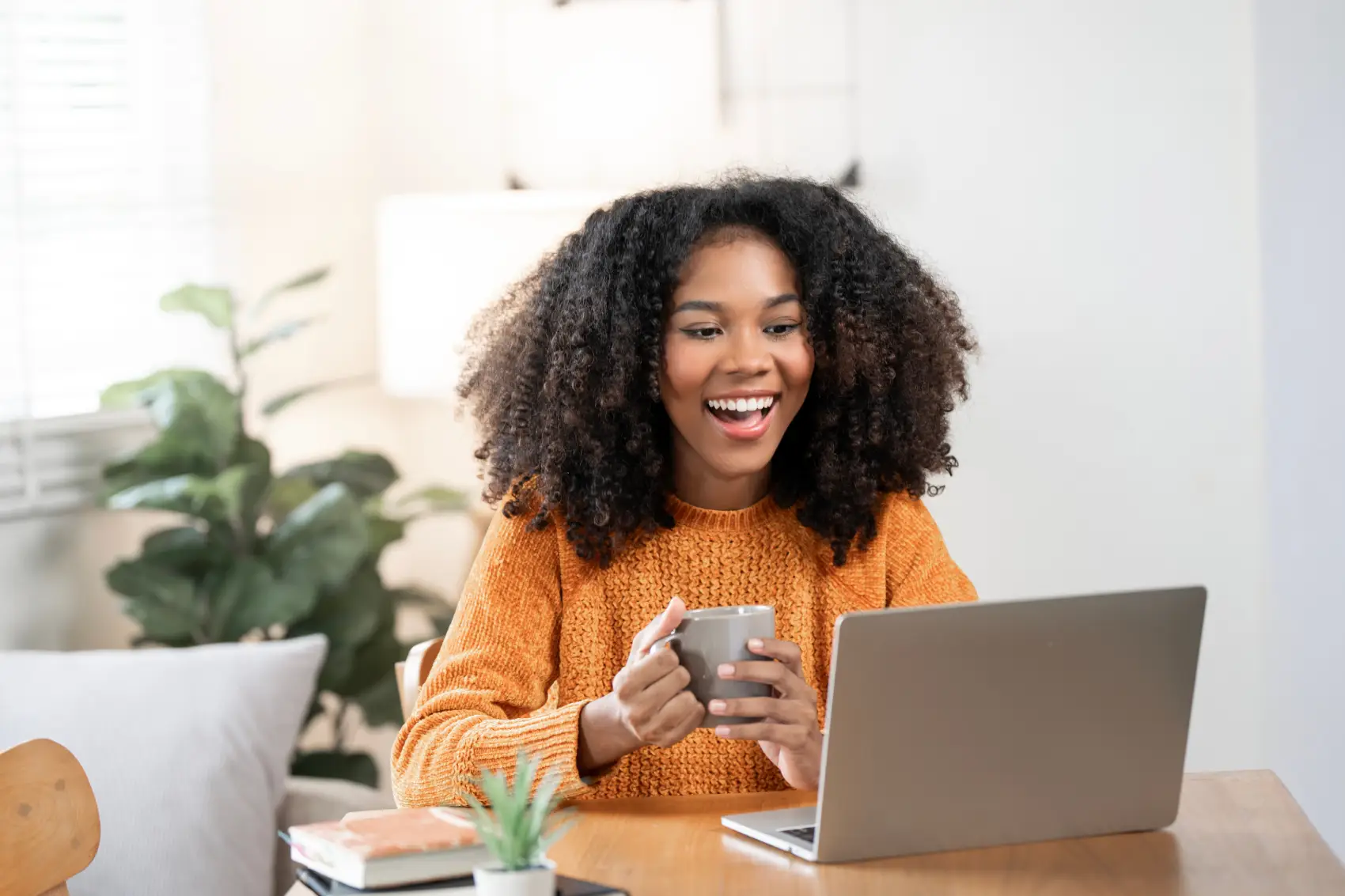 Lucro do FGTS - Mulher negra feliz desfrutando café da manhã enquanto usa laptop em casa.