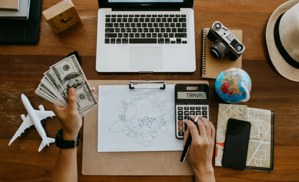 mesa com réplica de avião e notebook, e mão mexeno em uma calculadora