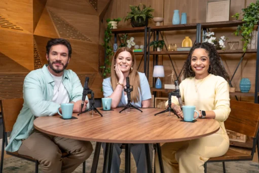 dicas para empreender - Eliezer, Viih Tube e Carol Gomes posam para a foto sentados em uma mesa redonda de madeira, em frente aos seus respectivos microfones