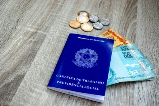 décimo terceiro salário - carteira de trabalho em mesa com notas de cem e cinqunta reais e algumas moedas de real