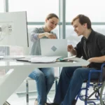 quem recebe bpc pode fazer empréstimo​ - Colegas de negócios, mulher e homem em cadeira para pessoas com deficiência trabalham no escritório