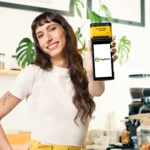 trocar maquininha pagbank - mulher caucasiana segurando maquininha pagbank Smart 2 sorrindo, olhando para a câmera