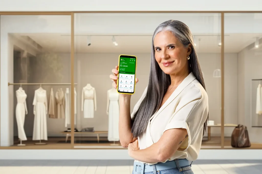 curso de trading - mulher mostrando app do celular em frente à sua loja de roupas