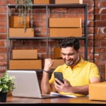 fim do elo7 - Homem indiano gerenciando pedidos online com laptop e smartphone, prontos para envio do armazém