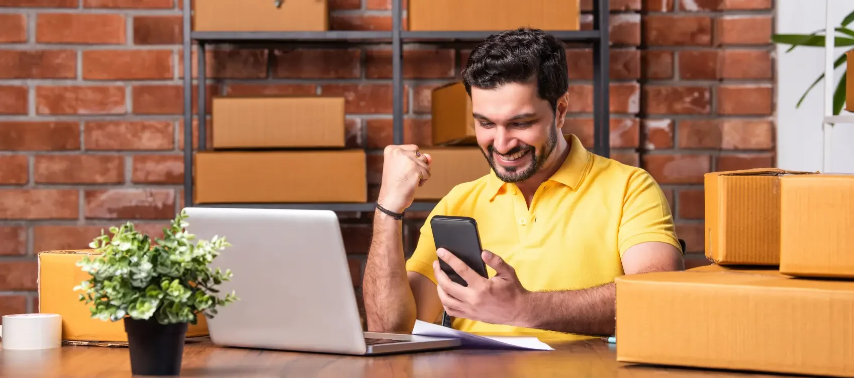 fim do elo7 - Homem indiano gerenciando pedidos online com laptop e smartphone, prontos para envio do armazém