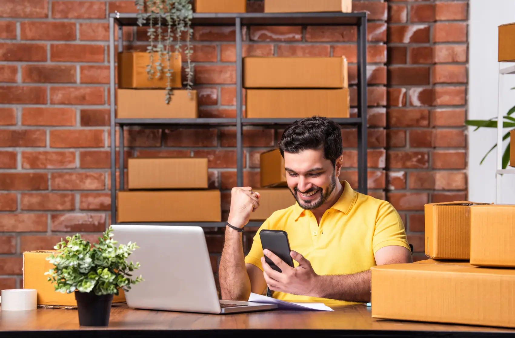 fim do elo7 - Homem indiano gerenciando pedidos online com laptop e smartphone, prontos para envio do armazém