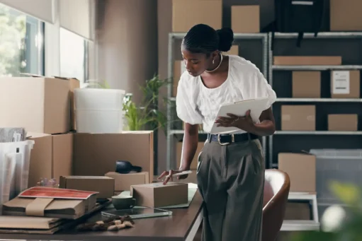 e-commerce-no-brasil - Comércio eletrônico, caixa e prancheta com mulher negra no armazém para transporte, distribuição e correio