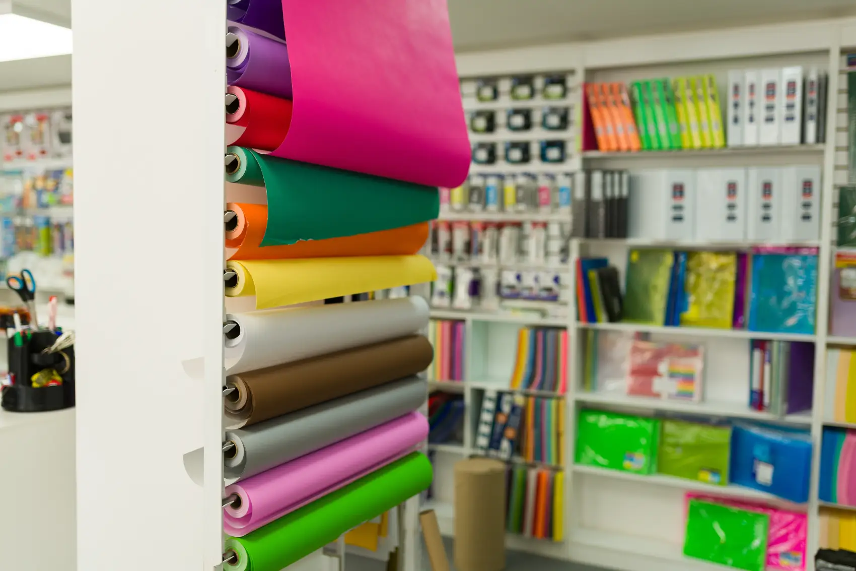 férias de julho - Exibição de rolos de papel coloridos em um rack com prateleiras desfocadas de vários itens de papelaria e material de escritório em segundo plano