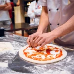 como-abrir-uma-pizzaria O pizzaiolo prepara a pizza Margherita. Ele amassa a massa com as mãos, adiciona molho de tomate e queijo mussarela. Comida tradicional italiana.