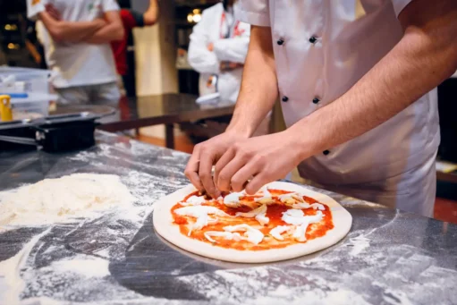 como-abrir-uma-pizzaria O pizzaiolo prepara a pizza Margherita. Ele amassa a massa com as mãos, adiciona molho de tomate e queijo mussarela. Comida tradicional italiana.